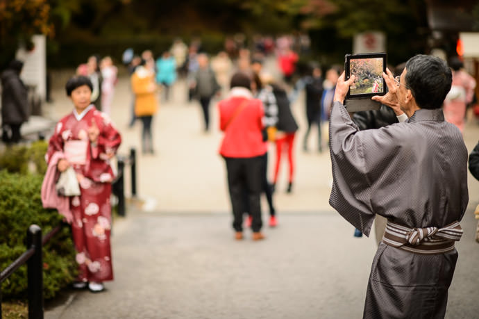 an elderly man in traditional Japanese kimono uses an iPad to photograph an elderly woman (presumably his wife) also in traditional Japanese kimono, at the Kiyomizu Temple (清水寺), Kyoto Japan