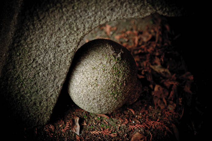 desktop background image of a stone sphere, tucked away haphazzardly under the legs of a stone lantern, in the back gardens of the Nishimura Stone Lantern stonecarving shop, Kyoto Japan -- Sphere -- Nishimura Stone Lantern workworkshopshop and garden -- Copyright 2009 Jeffrey Friedl, http://regex.info/blog/